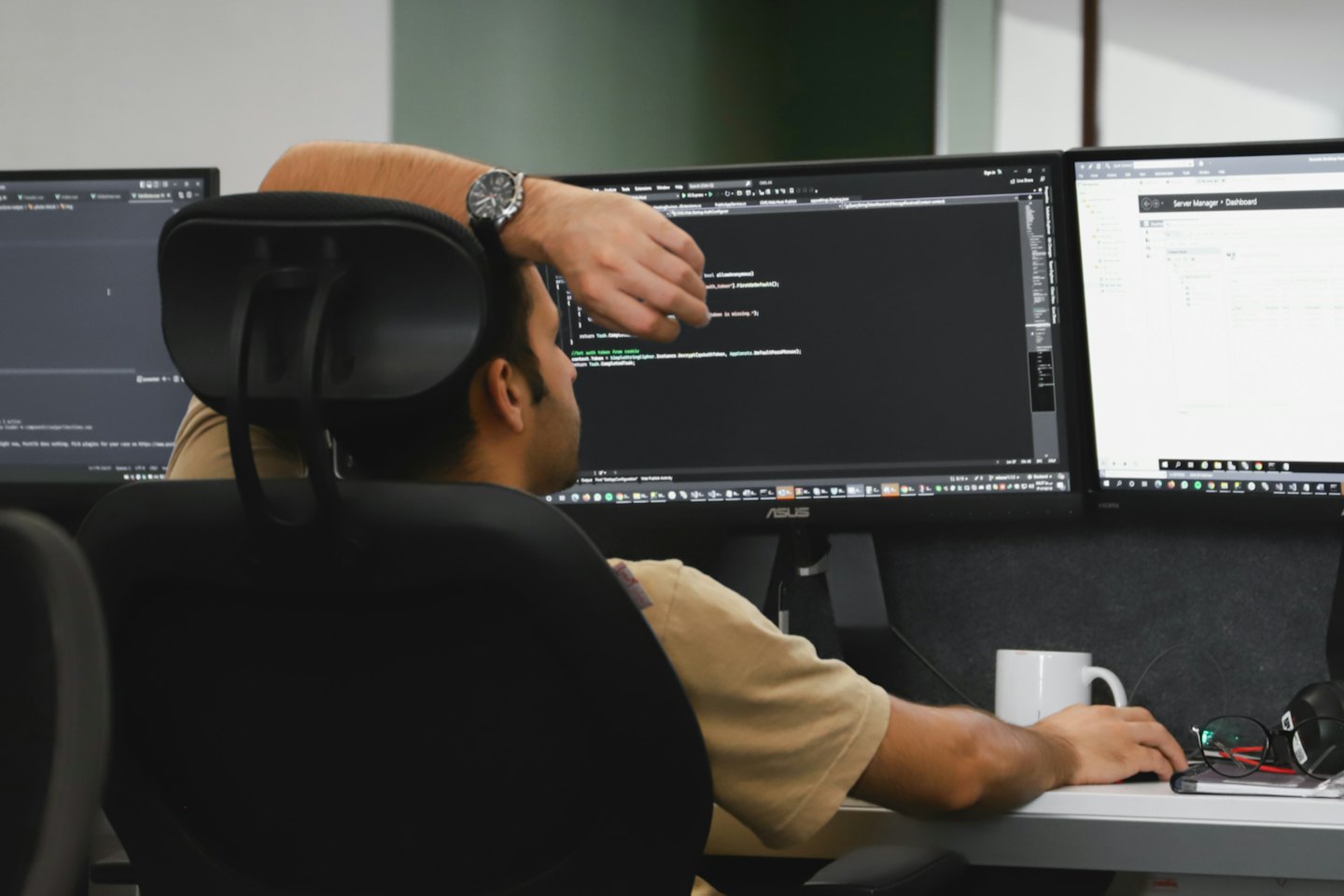 Man in beige shirt working on multi-monitor computer setup.